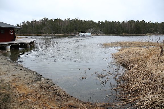 View of a small bay in Sweden, with a small house on the left shoreline and dry vegetation along the right side.