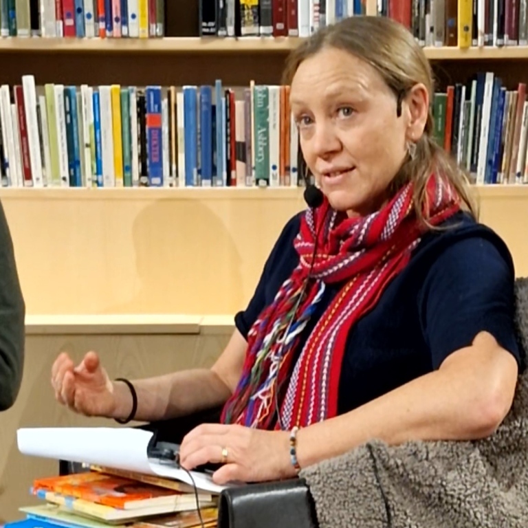 zanna Petersson Kero sitter med böcker i knät och med bokyllor i bakgrunden.