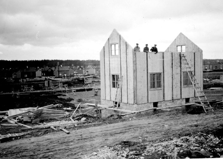 Svartvitt foto av tvåplansvilla i trä under uppbyggnad.