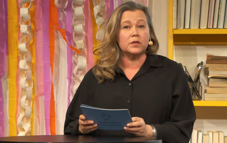Elina Druker står på en scen och läser en presentation