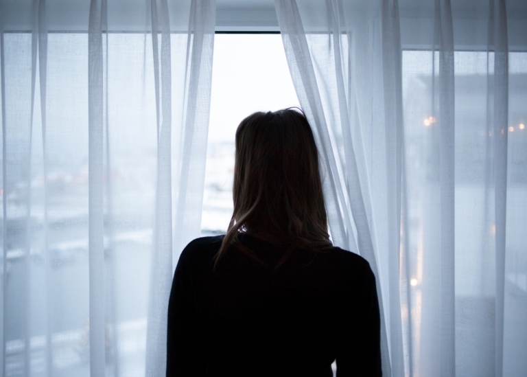 Siluett av kvinna som står i ett fönster och tittar ut