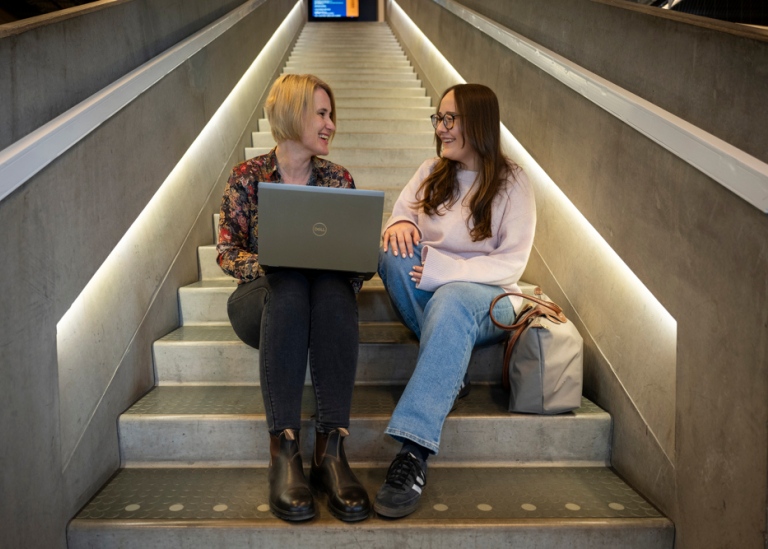 Examenshandläggare med student i trappan i Studenthuset.