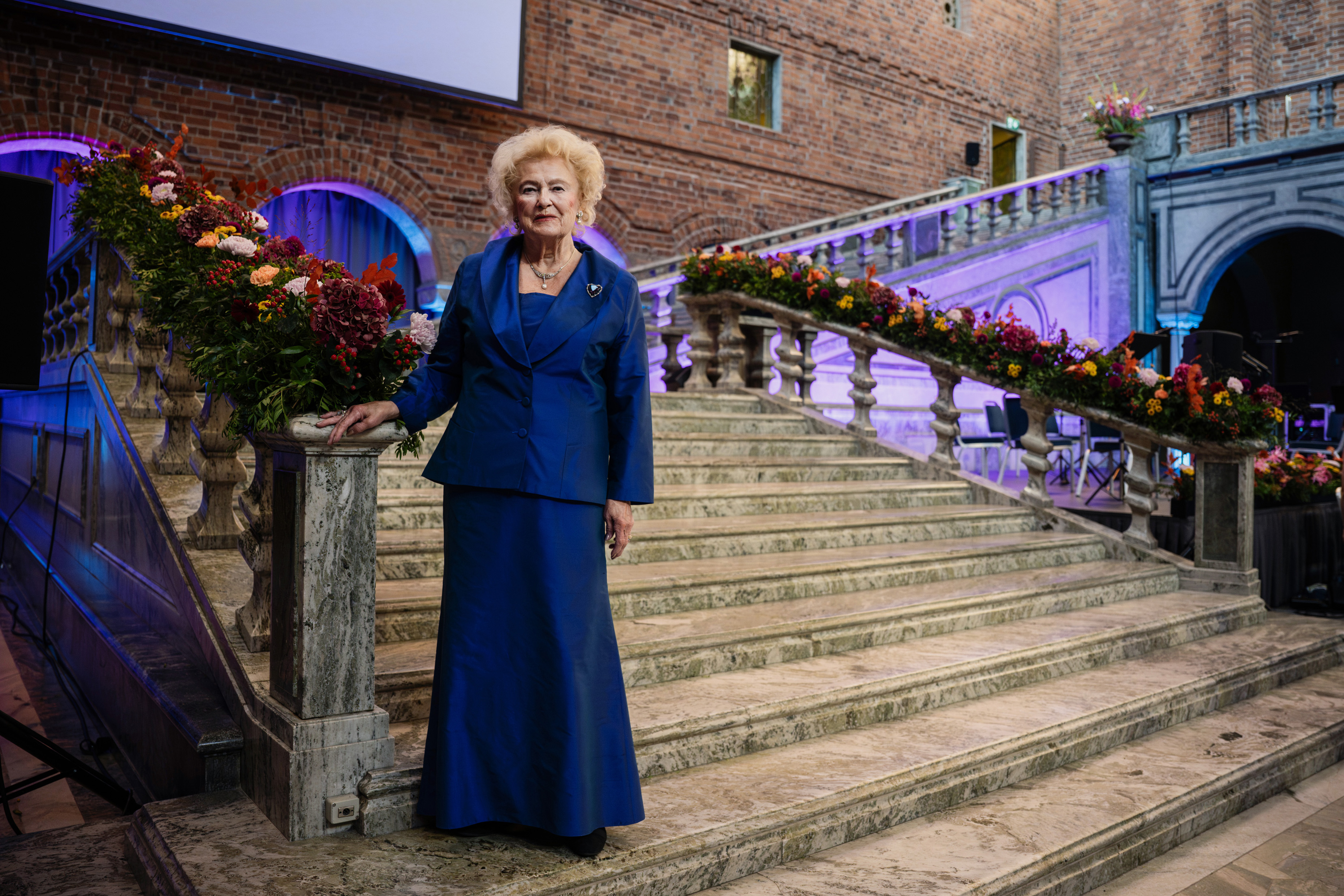 Kvinna i blå aftonklänning poserar i stentrappa vackert dekorerad med höstblommor.