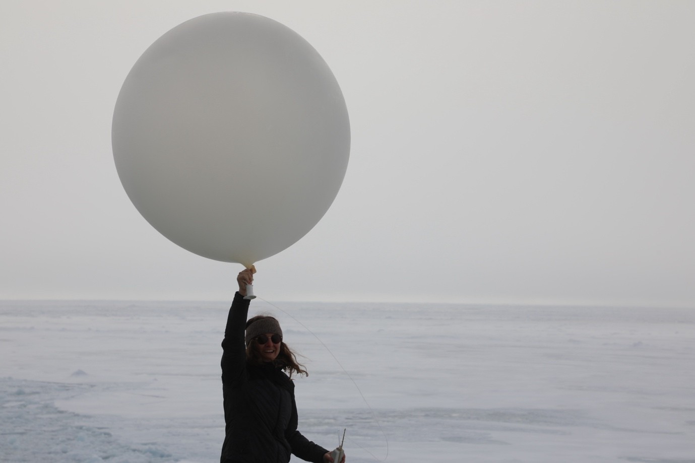 Woman holding a large gray-white balloon over her head, ready to release.