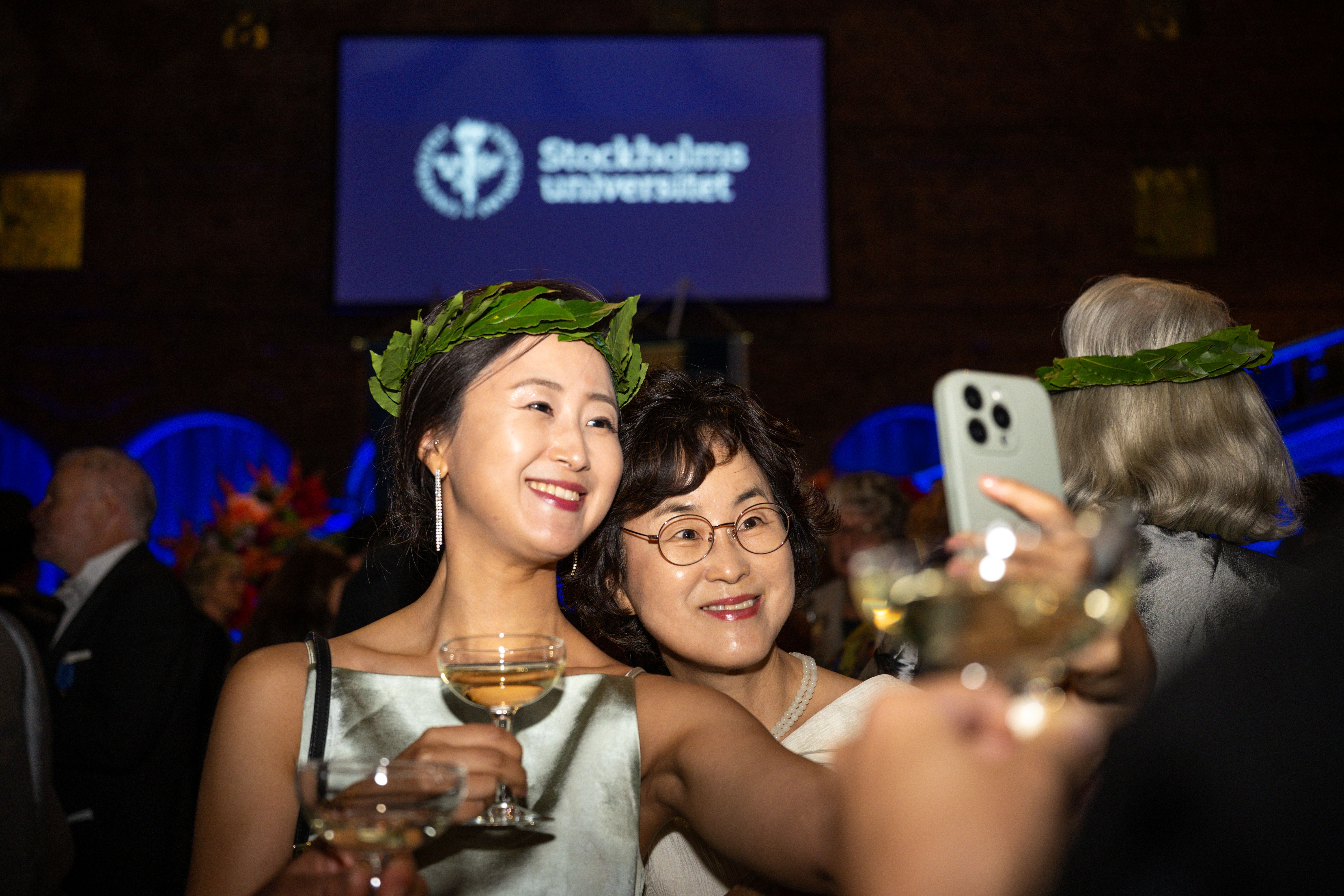 Kvinna med lagerkrans och glas i hand tar en selfie tillsammans med en väninna