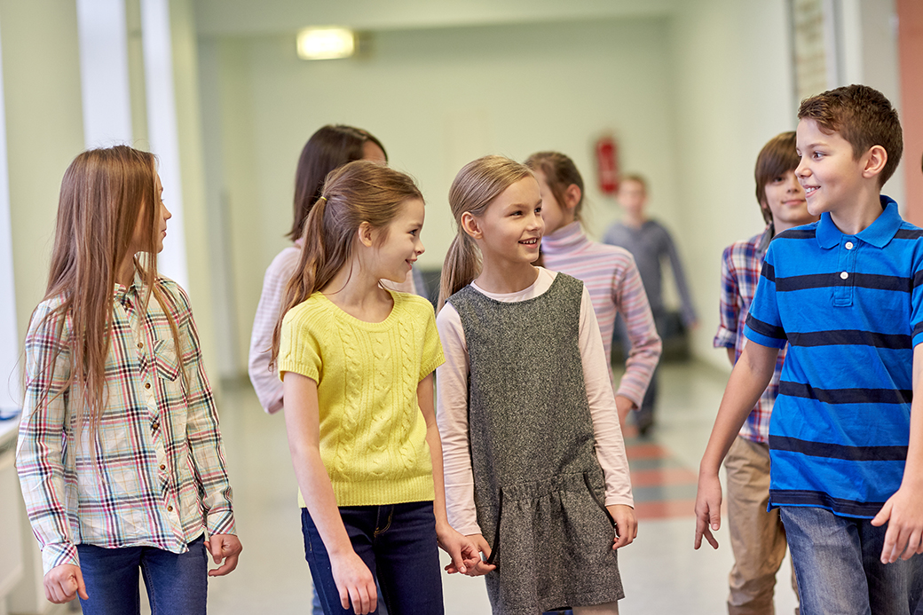 En grupp leende skolbarn, flickor och pojkar, som går i en skolkorridor.