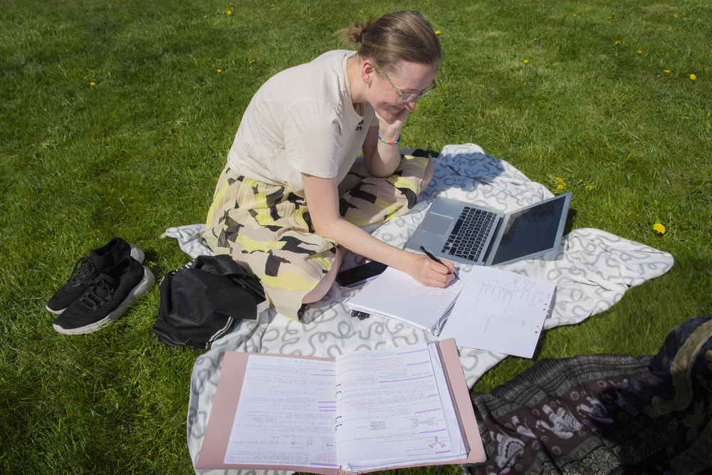 Student sitter på gräsmatta och pluggar. Foto: Ingmarie Andersson.