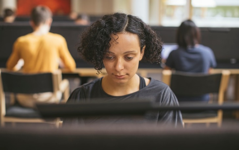 En student som sitter och studerar i ett rum med andra omkring sig