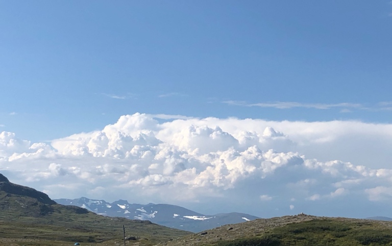 Clear blue sky and heavy white clouds over mountains.