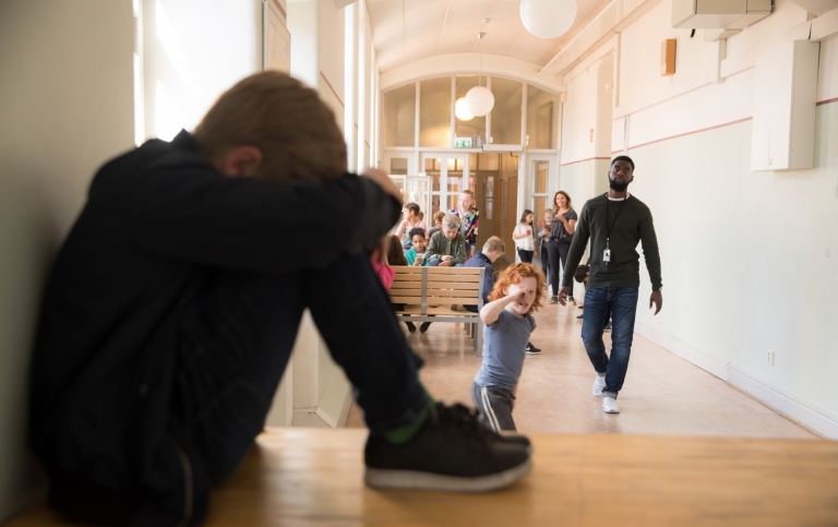 Ledsen pojke sitter i ett hörn i korridoren på en skola.