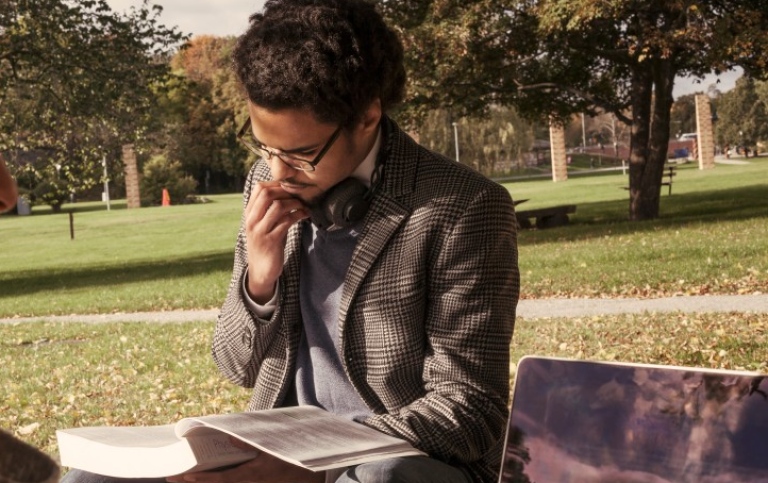 Student sitting on a bench outdoors reading.