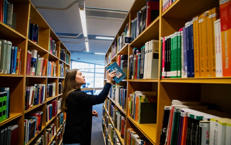 Student tar ut bok ur bokhylla i universitetsbiblioteket.