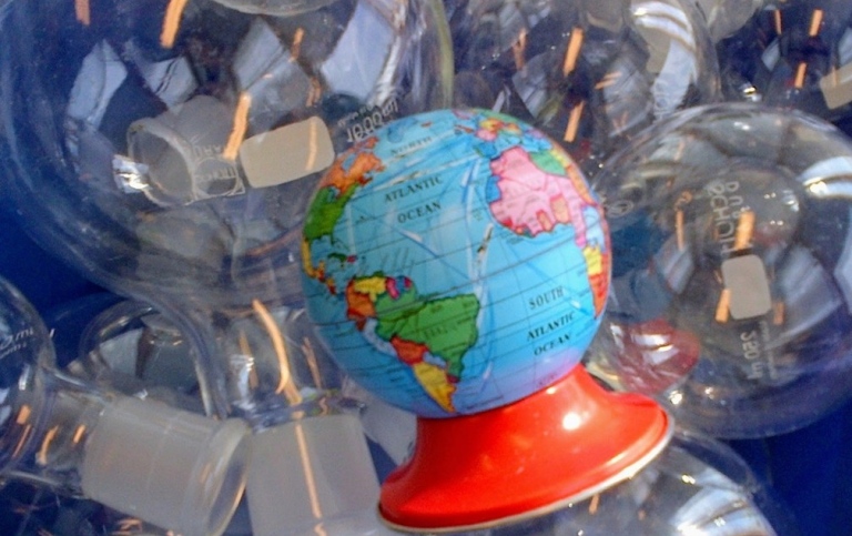 A small globe with a red base among glass laboratory flasks reflecting light.