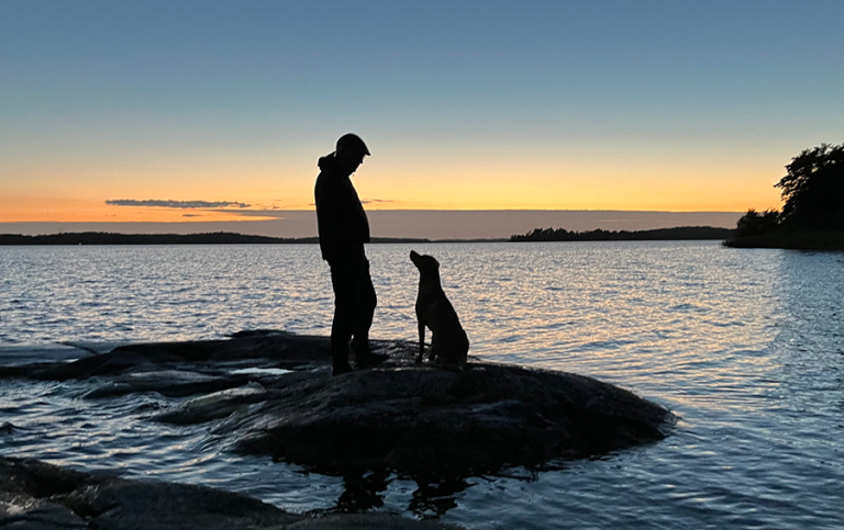 Siluett av man och hund invid en sjö