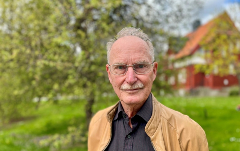 Bjarne Däcker. I bakgrunden syns grönskande träd och ett falurött hus skymtar.