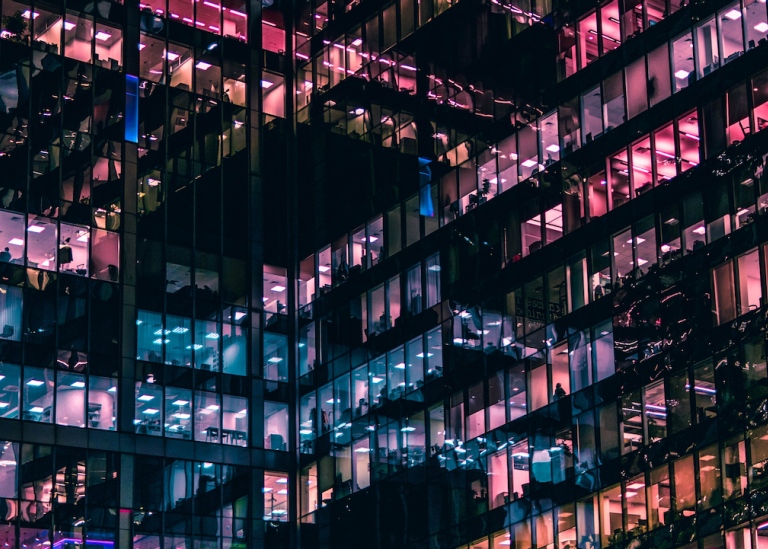 Genre photo: Office building with many floors, rooms lit in different colors. Illustrates research.