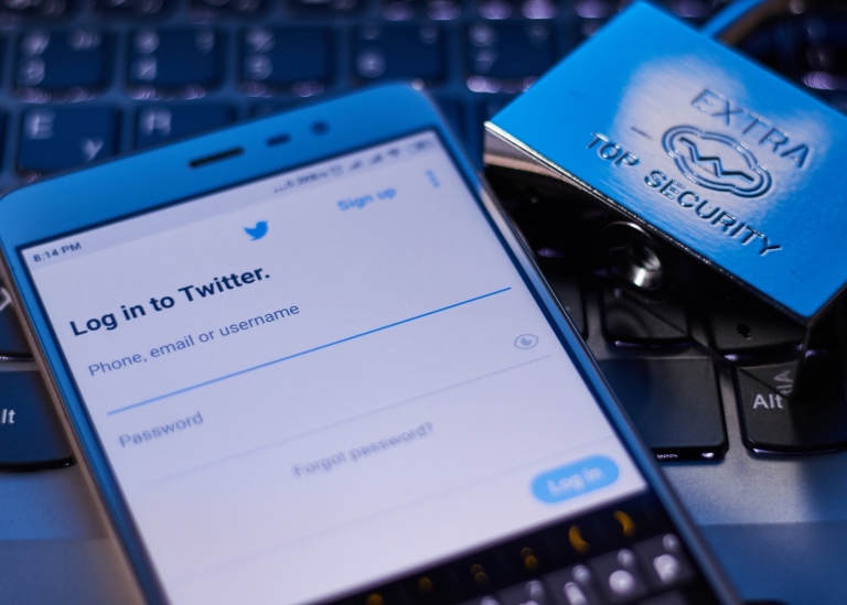 Mobile phone rests on keyboard with a lock next to it. Twitter login page appears on the screen