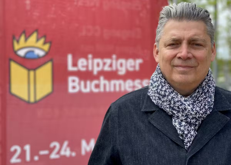 Le journaliste et auteur Michel Jean, devant une affiche de la Foire du livre de Leipzig