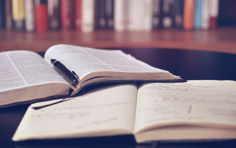 Öppen bok och anteckningsblock på biblioteket