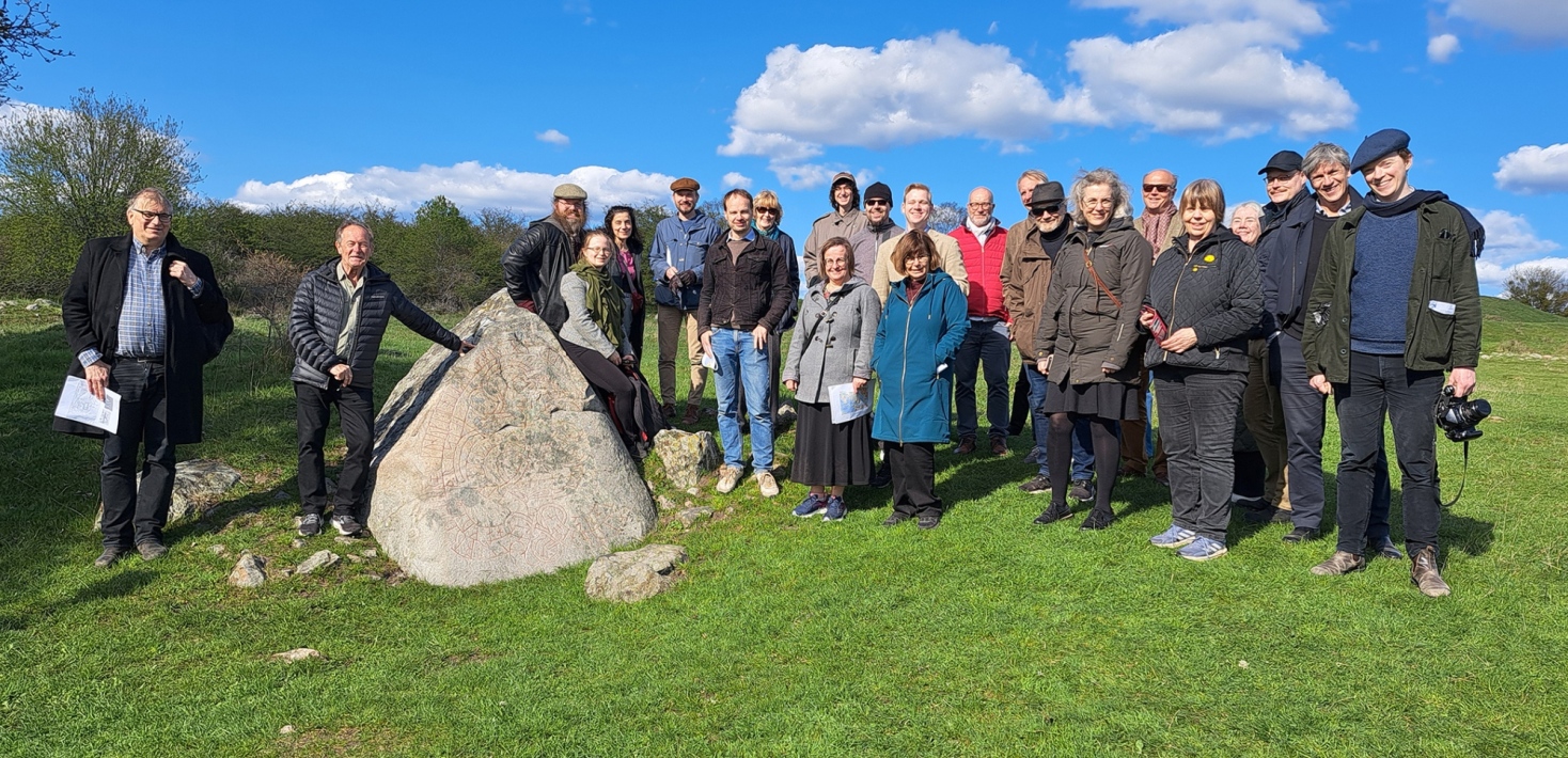 En grupp människor står framför en runsten.