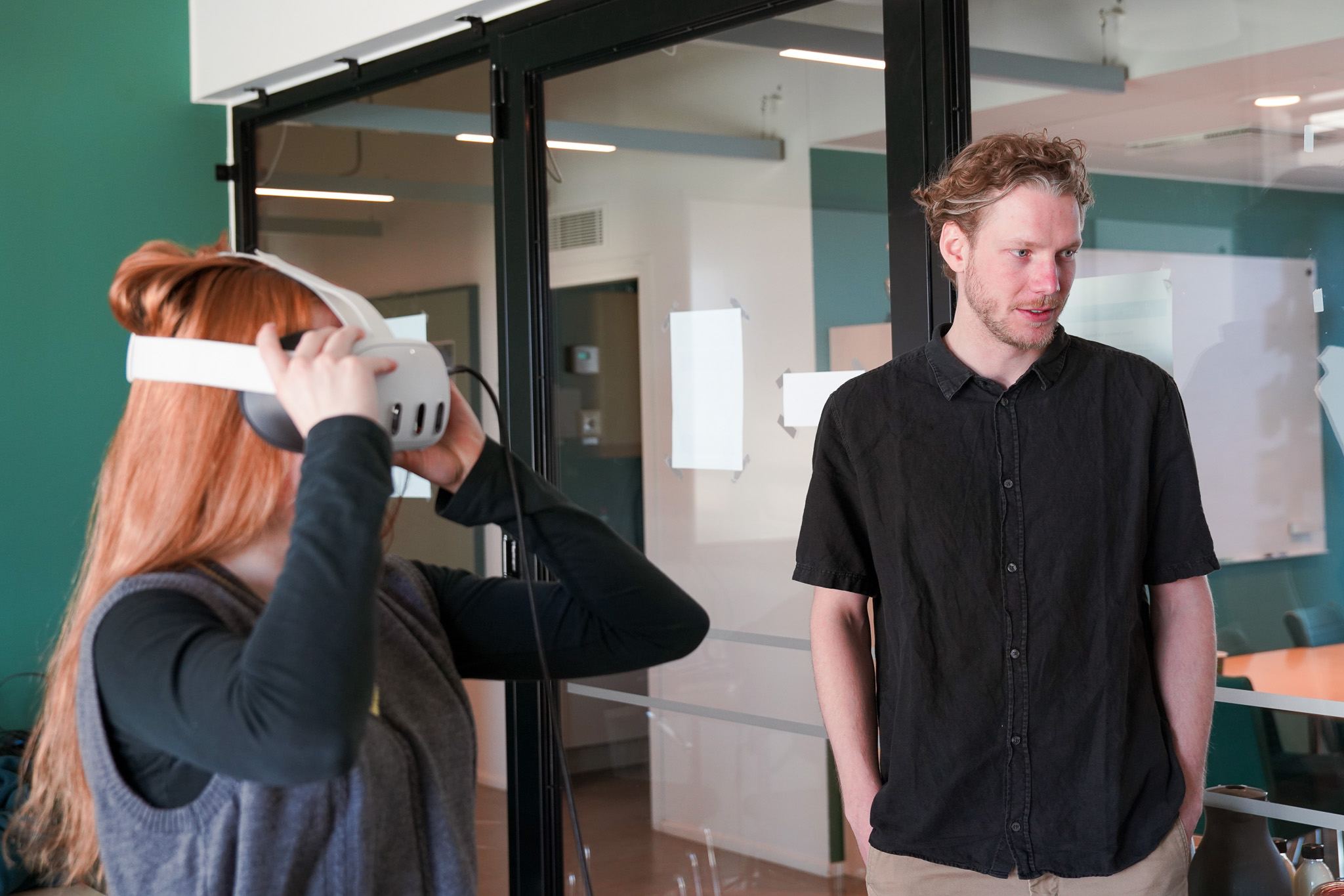 Visiting researcher Olivia Mostow tries IDaVIE during a session at the Oskar Klein Centre, with master's student Florian Unger pointing out a structure on the desktop monitor. The screen shows the Manticore reconstruction of a patch of the local universe; the controller is painting directly into that volume inside the headset.