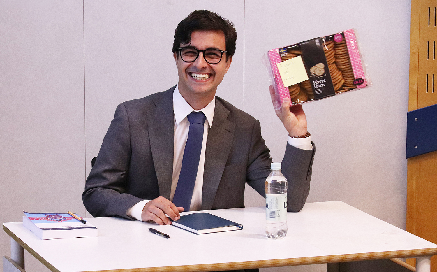 Tiago at his defense, sitting at a desk smiling holding up a gifted box of cookies.