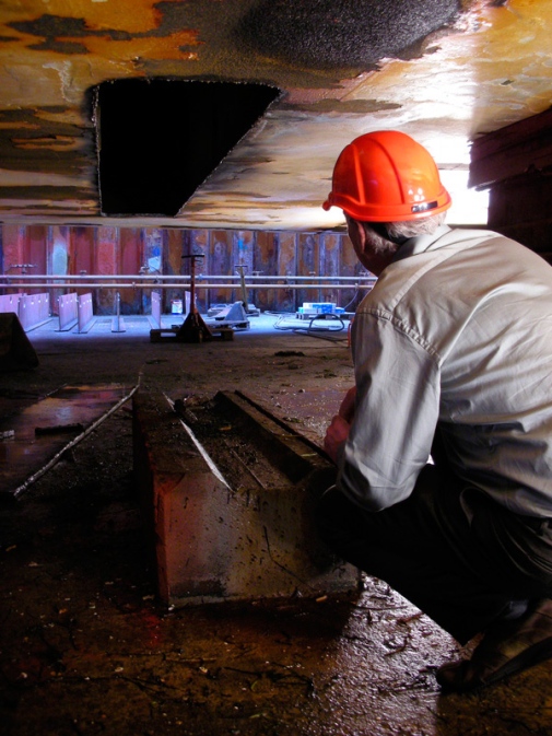 man crouching looking at hole in icebreaker hull