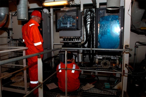 Two men looking into machines that look like a refrigerator, microwake thing