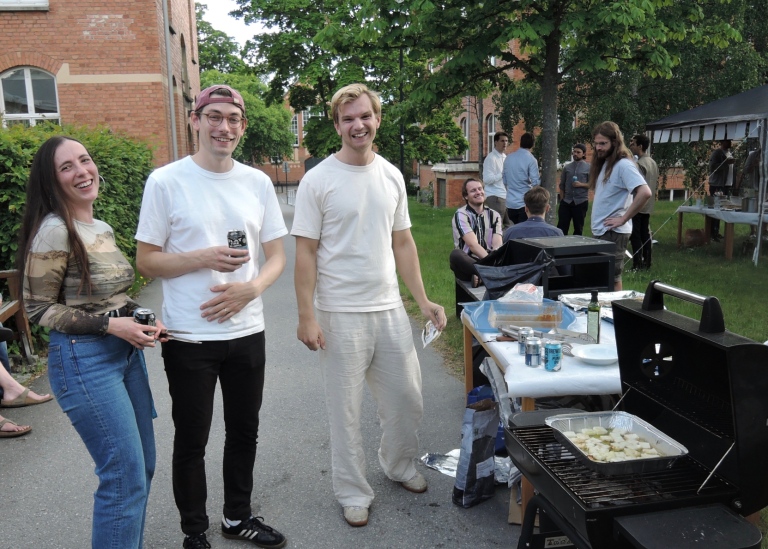 Sommarfest utomhus, tre personer vid grill i förgrunden.