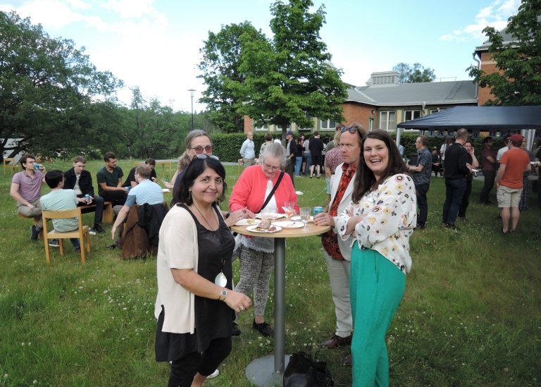 Sommarfest utomhus, fem personer vid ståbord i förgrunden.