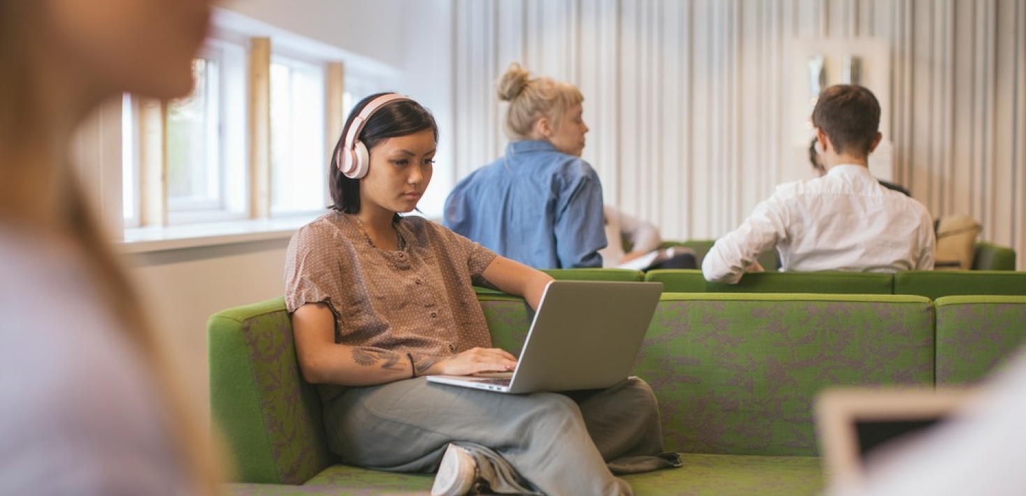 Student with laptop and earphones sitting in sofa