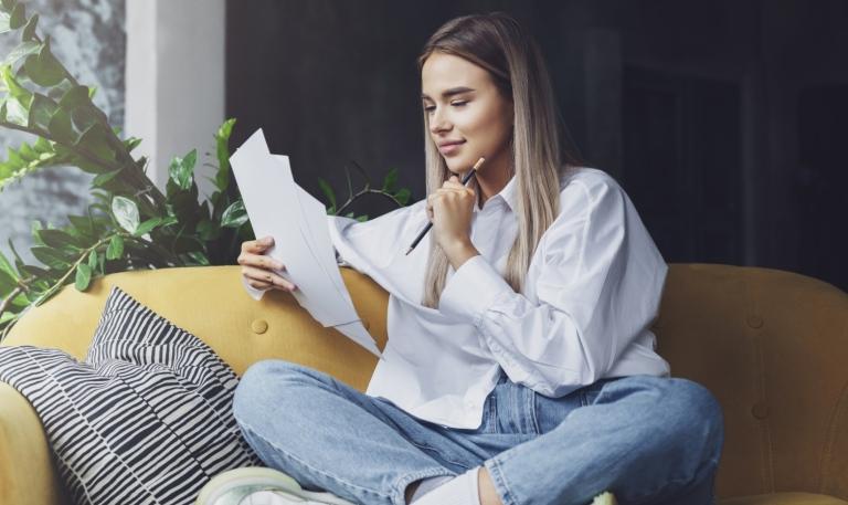 Ung student sitter i uppkrupen i en modern soffa och läser ett PM.