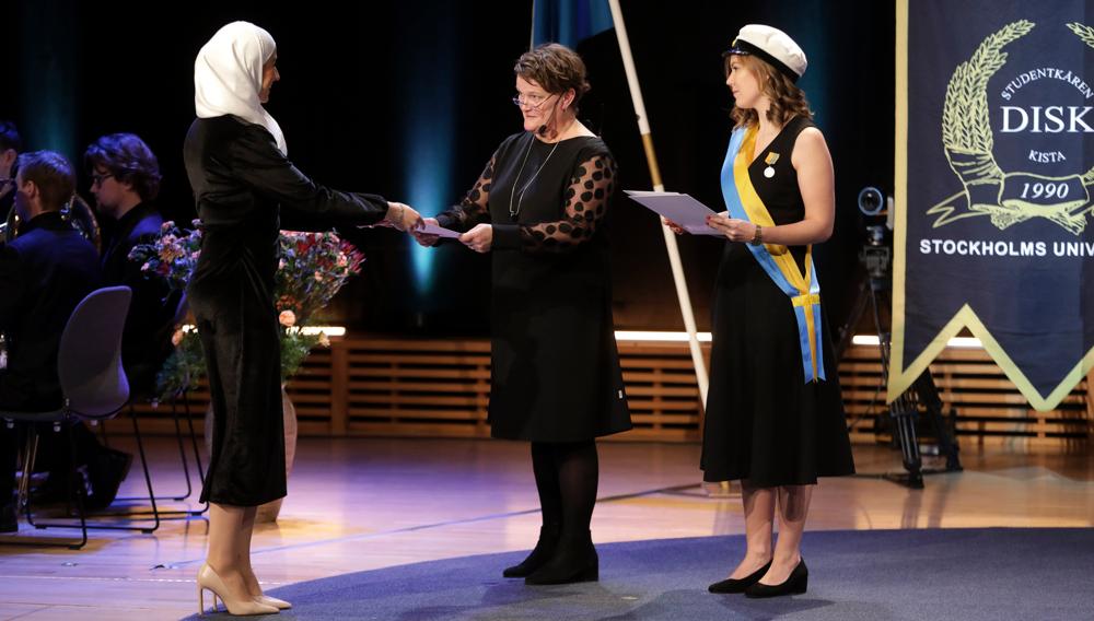 A woman receives a diploma from another woman. To the left there is third woman holding a diploma.