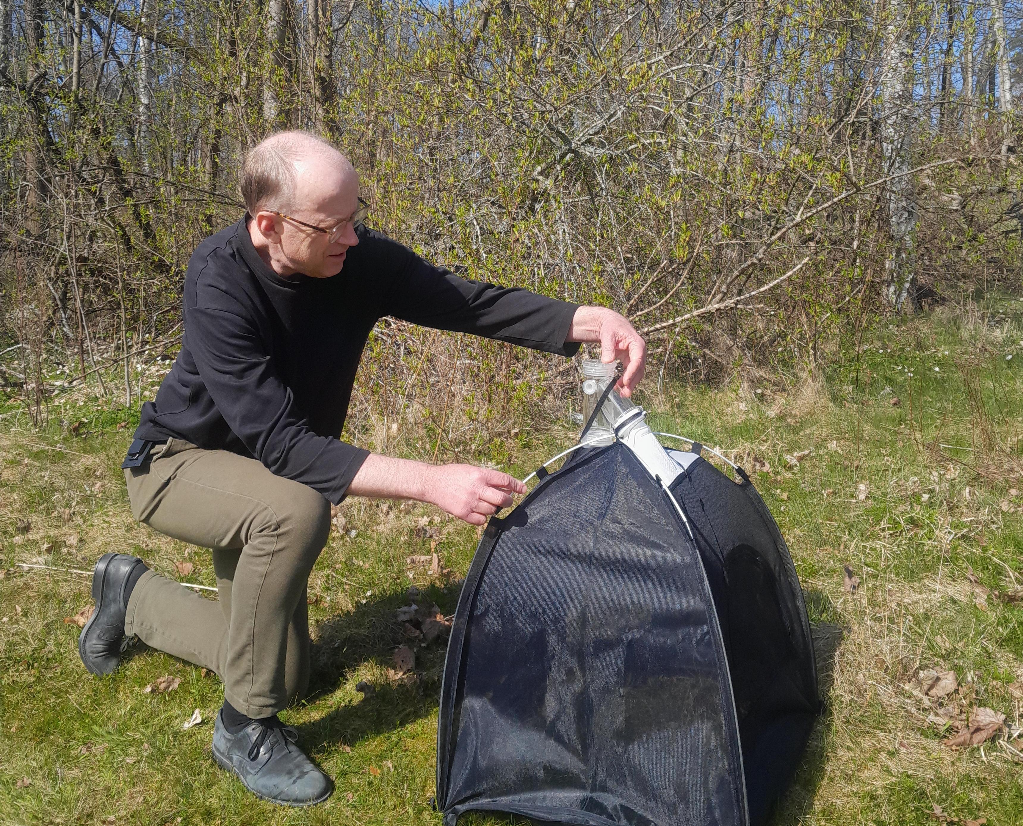 A man, crouching beside an emergence trap in a field.