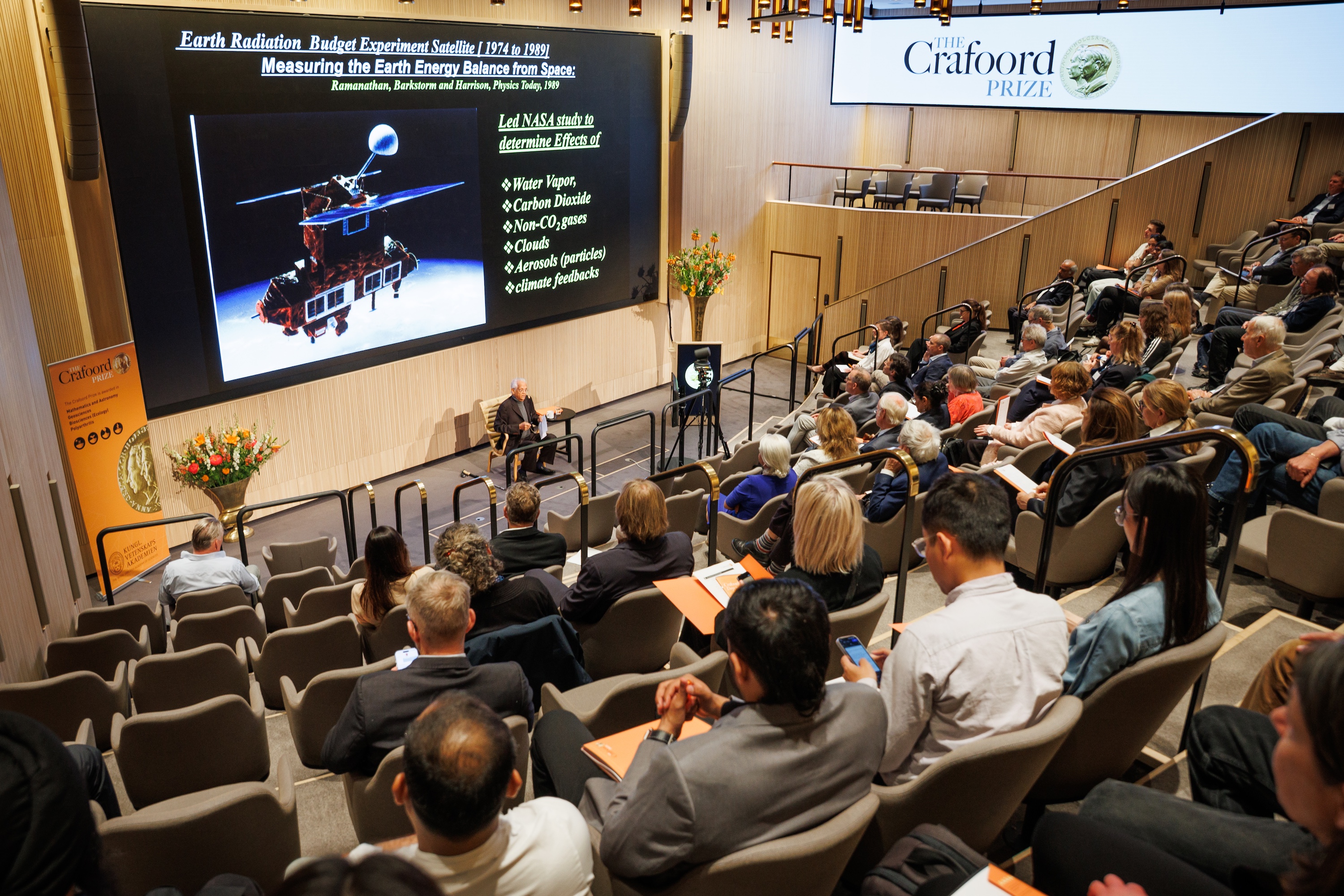 View from the back of a lecture hall showing attendees seated and facing Professor Veerabhadran as he gives a lecture at the front of the room.