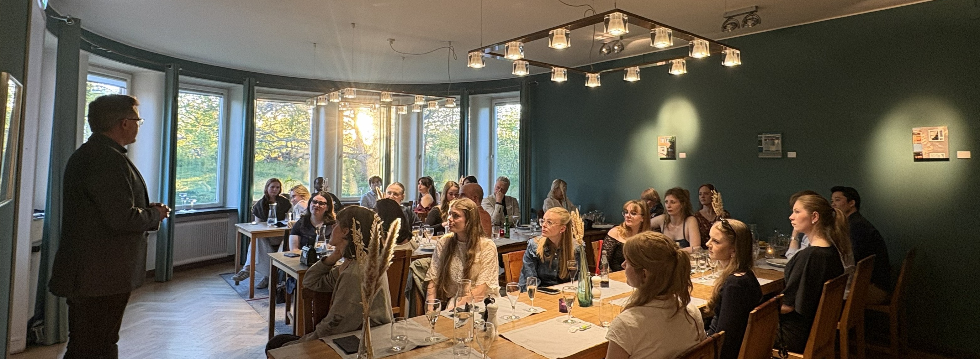 A man standing in front of young men and women sitting at tables.