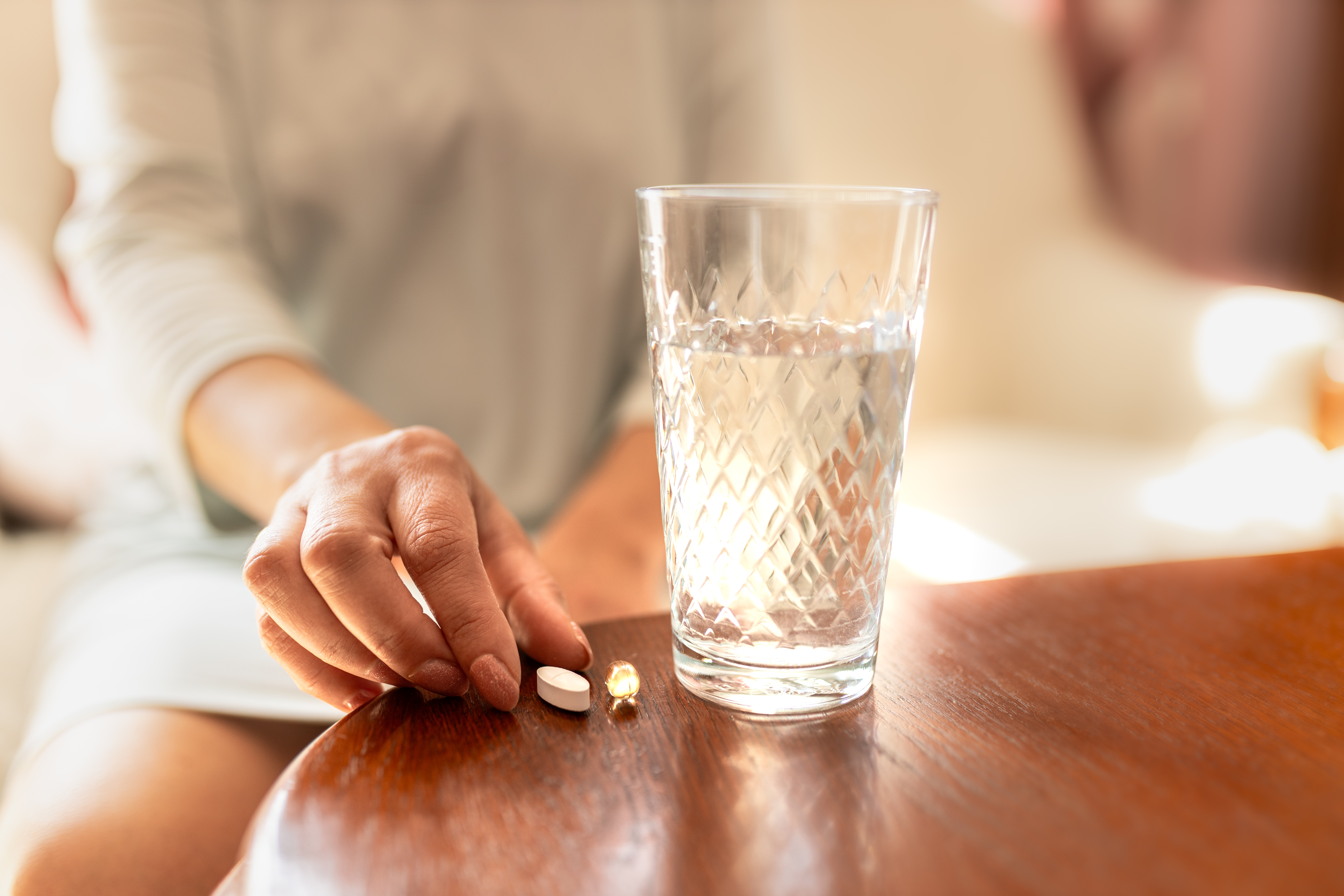 Woman´s hand reaching for a pill beside a glass of
water on a table.