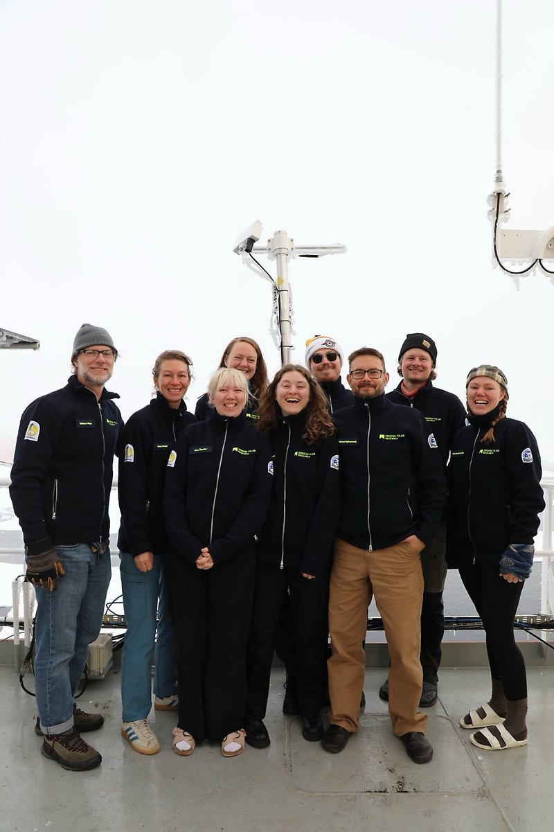 Bildtext: Gruppfoto på samtliga deltagare från SU på däck 7 vid Nordpolen (från vänster: Matthew Shupe (MISU), Hanna Winge (MISU), Alva Åkerlind (IGV), Linnea Huusko (MISU), Irene Bellagente (ACES), Albin Eriksson (ACES), Richard Gyllencreutz (IGV), Rune Bech Pedersen (IGV), Miriam De Vries (naturgeografi). Matthew O'Regan (IGV) saknas på bilden).