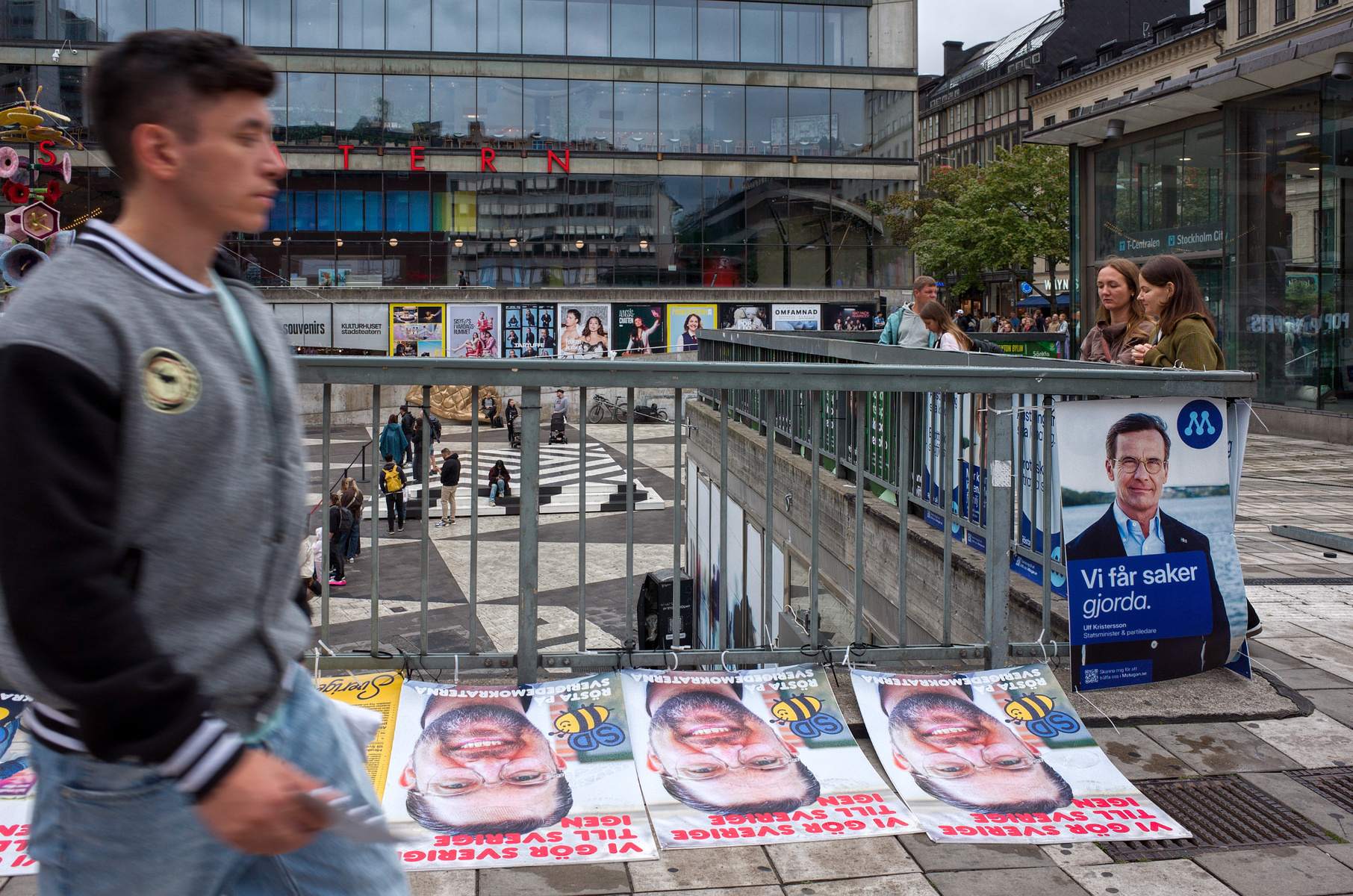 En ung man går förbi valaffischer vid Sergels torg.