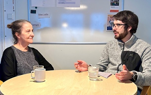 Eva Nobel och Roger Cattaneo sitter och samtalar vid ett runt bord med koppar och glas.