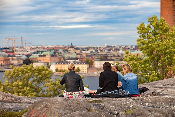 Fyra kvinnor sitter på en klippavsats och tittar ner på staden.