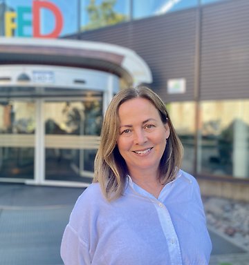 Susanne i vit skjorta framför entrén till Södra husen
