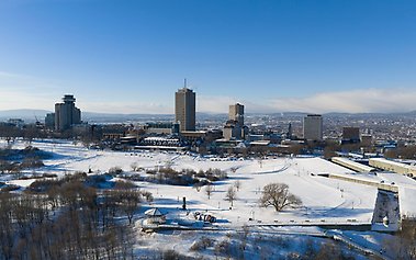Panoramavy över Québec City under vintern, med snötäckt parkmark i förgrunden och stadens skyline med höghus i bakgrunden under klarblå himmel.The skyline of Quebec City, Canada, pictured in January 2026.