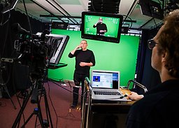 Person står bland kameror och tecknar med green screen i bakgrunden.