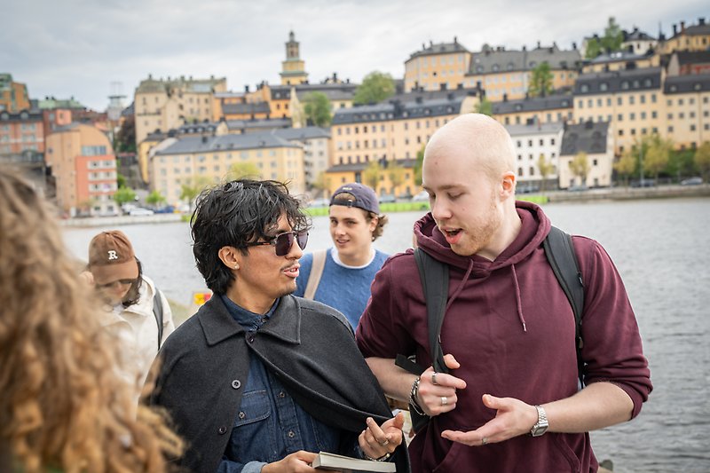 Studenter i stan med vatten och byggnader i bakgrunden.