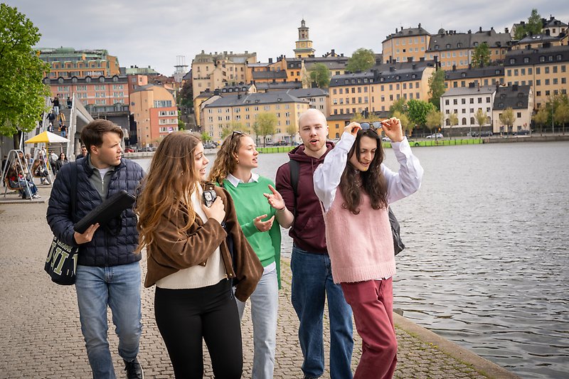 Studenter i stan med vatten och byggnader i bakgrunden.