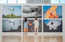 Två personer observerar olika konstverk i en modern konstgallerimiljö.
