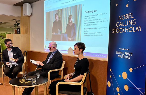 Paneldeltagare på bibliotekets scen med direktsändningen från Börshuset i bakgrunden.