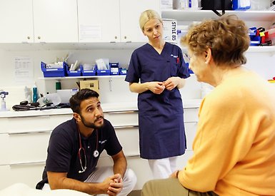 Läkare och sjuksköterska pratar med en äldre patient i ett undersökningsrum.