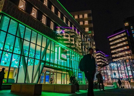Enstaka personer står utanför en upplyst kontorsbyggnad på kvällen.